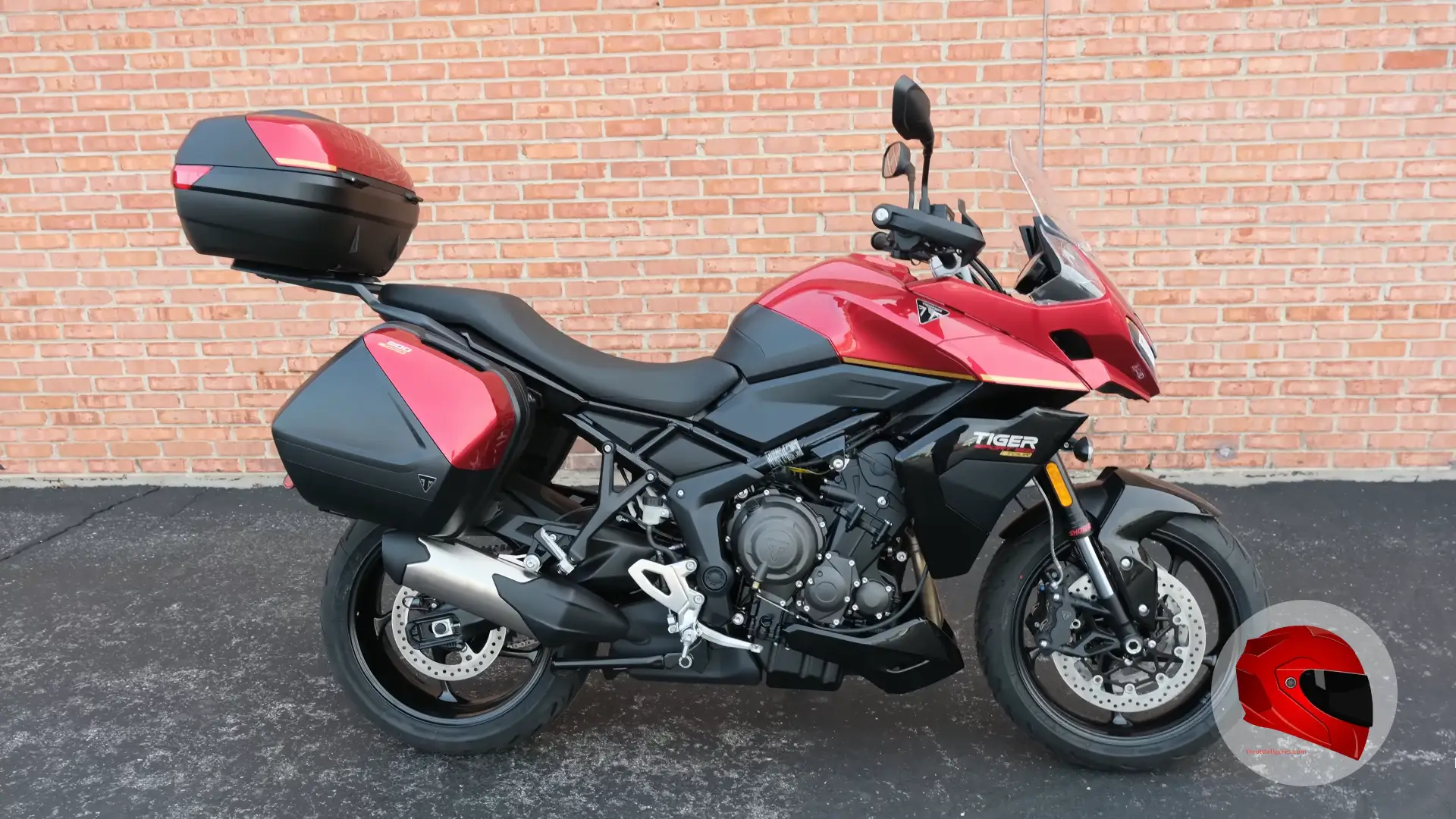 Red adventure motorcycle with luggage parked against a brick wall