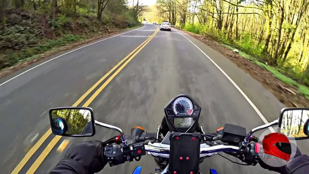Rider's view from a Suzuki SV650 on a winding road, showing the handlebar, mirrors, and speedometer